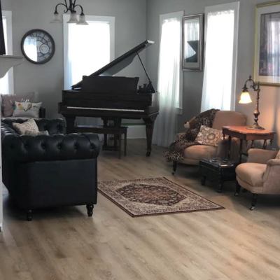 A classic living room with a grand piano, Chesterfield sofa, beige armchairs, and an Oriental-style rug on light wood flooring.